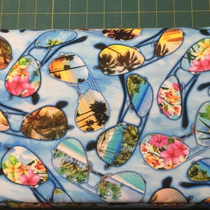 May include: Fabric with a repeating pattern of sunglasses. The lenses feature tropical scenes with palm trees, flowers, and beach views. The sunglasses are set against a light blue background.