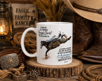 May include: A white ceramic mug featuring a graphic of a person riding a bucking horse. The text reads: I CAN DO ALL THINGS Through Christ WHO STRENGTHENS ME. BE STRONG & COURAGEOUS DO NOT BE AFRAID DO NOT BE DISCOURAGED for the Lord your God WILL BE WITH YOU WHEREVER YOU GO. JOSHUA 1:9.