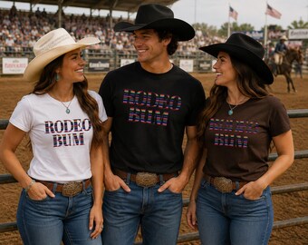 May include: Three t-shirts in white, black, and brown, each featuring the text RODEO BUM in a colorful striped pattern. The shirts are paired with blue denim jeans and large metallic belt buckles, complemented by cowboy hats in white and black.