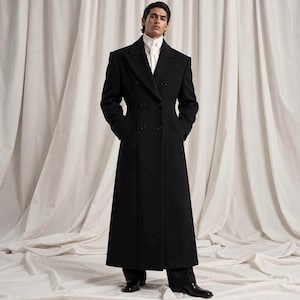 Puede incluir: Un abrigo largo negro de doble botonadura con solapas anchas y hombros estructurados, usado sobre una camisa blanca de cuello alto. El abrigo presenta un corte entallado, mangas largas y un acabado negro sólido que llega hasta los tobillos.