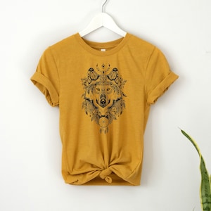 May include: A mustard yellow t-shirt with a black and white graphic of a wolf's head with dreamcatcher elements.