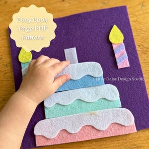 May include: A purple felt square featuring a multi-layered cake craft project with white frosting accents, two separate candle shapes, and a small velcro tab. The text Busy Book Page PDF Pattern is visible in a light yellow scalloped graphic.