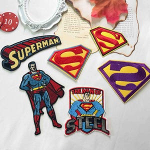 Może przedstawiać: Kolekcja haftowanych naszywek z motywami Supermana, w tym klasyczna czerwono-żółta tarcza z literą S, pełna postać bohatera, emblemat Man of Steel oraz naszywka z żółto-czarnym napisem Superman.