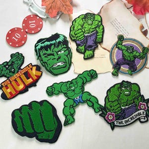 May include: A collection of embroidered fabric patches featuring the green character Hulk in various poses, including a large fist, a close-up face, and full-body action stances. One patch displays the text THE INCREDIBLE HULK in yellow letters.