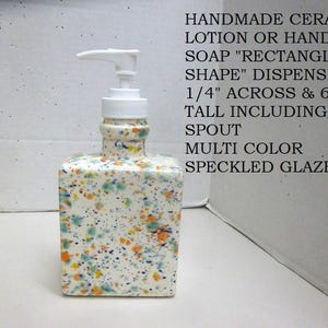 May include: A rectangular ceramic lotion or hand soap dispenser with a white base and multi-color speckled glaze. It features a white pump mechanism and measures 3 1/4 inches across and 6 3/4 inches tall including the spout.