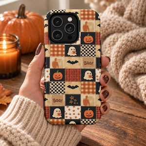 Könnte beinhalten: Eine Smartphone-Hülle mit einem Patchwork-Gitterdesign aus abwechselnden Quadraten in orange-schwarzem Karomuster, Schachbrettmustern und Unifarben. Das Design enthält Illustrationen von Geistern, Kürbissen, Fledermäusen, Sternen und dem Text Boo!.