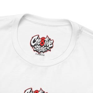Può includere: Una t-shirt bianca con un logo in stile graffiti nero, bianco e rosso sul bordo interno del collo che riporta la scritta Cre8tive Style. Sotto il testo, sono stampate piccole icone nere per la cura del capo all'interno del colletto.