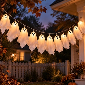 May include: A string of white ghost-shaped lights hanging outdoors. Each ghost is made of a translucent fabric with two black oval eyes and a black oval mouth. The lights emit a warm yellow glow, illuminating the figures against the evening sky.