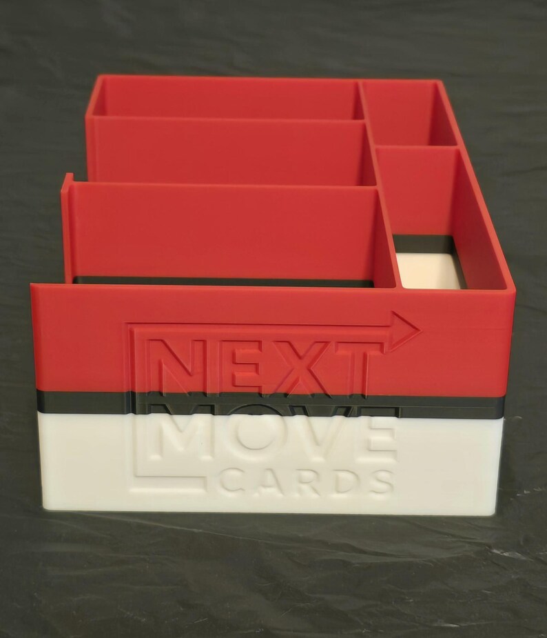 Puede incluir: Un organizador de tarjetas rectangular de pl&aacute;stico rojo, negro y blanco con m&uacute;ltiples compartimentos interiores. El exterior frontal presenta el texto en relieve NEXT MOVE CARDS con una flecha hacia la derecha sobre las secciones roja y blanca.