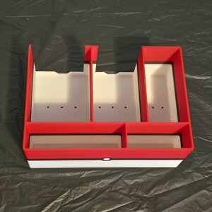 Puede incluir: Un organizador de almacenamiento rectangular de pl&aacute;stico con una secci&oacute;n superior roja y una secci&oacute;n inferior blanca separadas por una fina l&iacute;nea horizontal negra. El interior est&aacute; dividido en cinco compartimentos de tama&ntilde;os variados.