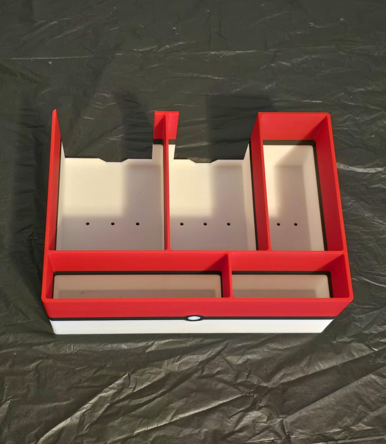 Puede incluir: Un organizador de almacenamiento rectangular de pl&aacute;stico con una secci&oacute;n superior roja y una secci&oacute;n inferior blanca separadas por una fina l&iacute;nea horizontal negra. El interior est&aacute; dividido en cinco compartimentos de tama&ntilde;os variados.