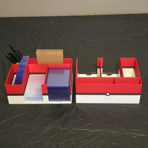 Puede incluir: Dos organizadores de almacenamiento rectangulares con un dise&ntilde;o en rojo, blanco y negro con un detalle circular en el frente. El organizador izquierdo contiene marcadores negros, fundas de pl&aacute;stico transparente y tarjetas marrones.