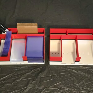 Puede incluir: Dos organizadores rectangulares de pl&aacute;stico en rojo, blanco y negro con m&uacute;ltiples compartimentos. El organizador izquierdo contiene marcadores negros, divisores de cart&oacute;n marr&oacute;n y fundas para tarjetas azules.