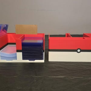 Puede incluir: Un organizador de almacenamiento de pl&aacute;stico rojo, blanco y negro con m&uacute;ltiples compartimentos. El dise&ntilde;o presenta una franja negra horizontal con un c&iacute;rculo blanco central, imitando una bola. Una secci&oacute;n contiene fundas de cartas azules.