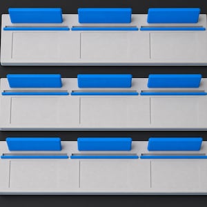 May include: Three rectangular light grey display stands, each featuring three distinct slots along the top edge. Each slot is fitted with a bright blue rectangular insert, creating a uniform arrangement of nine blue accents across the three stands.