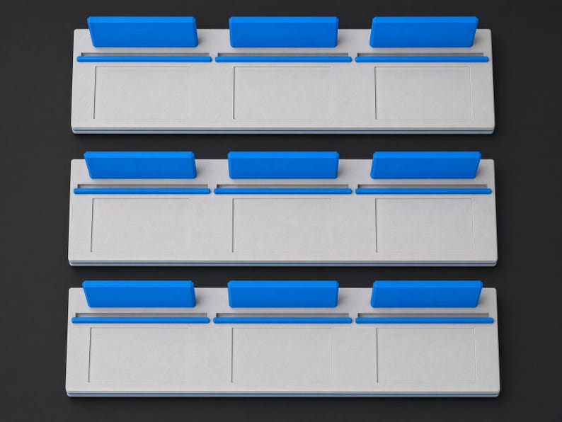 May include: Three rectangular light grey display stands, each featuring three distinct slots along the top edge. Each slot is fitted with a bright blue rectangular insert, creating a uniform arrangement of nine blue accents across the three stands.