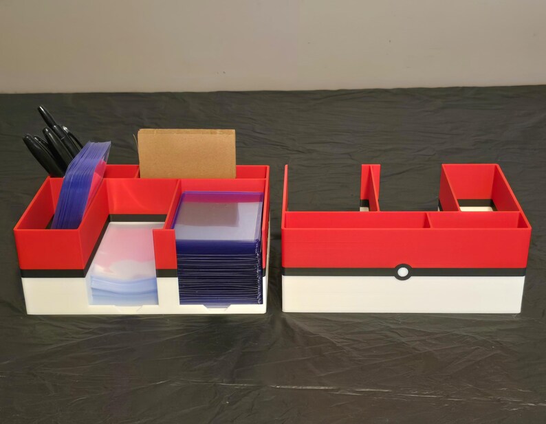 Puede incluir: Dos organizadores de escritorio rectangulares con un esquema de color rojo, blanco y negro con un detalle circular central. El organizador izquierdo contiene bol&iacute;grafos negros, fundas para tarjetas azules y un bloque rectangular marr&oacute;n.