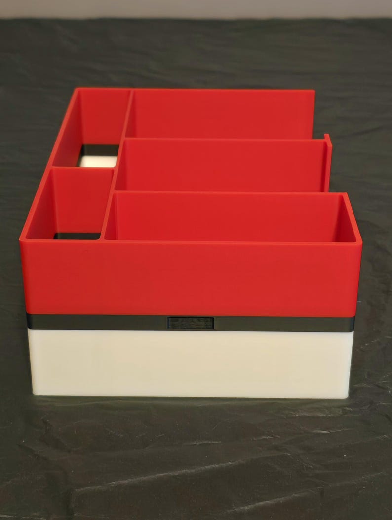 Puede incluir: Un organizador de escritorio rectangular que presenta una secci&oacute;n superior roja con m&uacute;ltiples compartimentos y una secci&oacute;n inferior blanca, separadas por una fina banda horizontal negra. La estructura est&aacute; dividida en varios espacios abiertos.