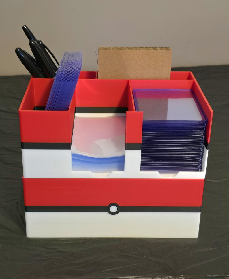 Puede incluir: Un organizador de escritorio de pl&aacute;stico rojo, blanco y negro con m&uacute;ltiples compartimentos. Contiene marcadores negros, una pila de fundas para tarjetas de pl&aacute;stico transparente azulado, un inserto de cart&oacute;n marr&oacute;n y tarjeteros r&iacute;gidos.