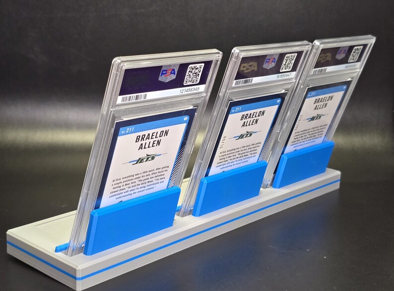 May include: Three Braelon Allen sports trading cards in clear PSA protective slabs, displayed upright in a light grey and blue plastic stand. Each card features the player's name, the Jets team logo, and text on the back, with a PSA logo at the top.