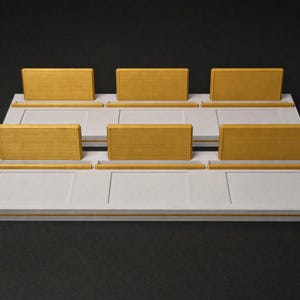 May include: Two rectangular white display bases, each featuring three raised yellow wooden rectangular panels and three corresponding yellow horizontal slots. The white bases have a smooth, flat surface with recessed rectangular outlines.