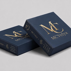 Peut inclure: Deux boîtes carrées bleu marine avec un marquage à chaud doré. Le dessus et le côté présentent le logo doré MC et le texte MCVelya. Le panneau latéral inclut le texte Creative Designs for Everyday Inspiration et un petit motif floral.