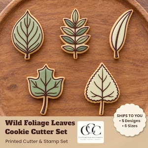 May include: A set of five leaf-shaped cookie cutters featuring various botanical designs with dark brown outlines. The text reads Wild Foliage Leaves Cookie Cutter Set, Printed Cutter & Stamp Set, and CustomCookieCutterCo.