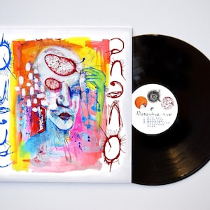 May include: A vinyl record with a colorful abstract painting on the cover. The painting features a face with multiple eyes and a hand reaching out. The record label says "Monster Side" and lists the track titles.