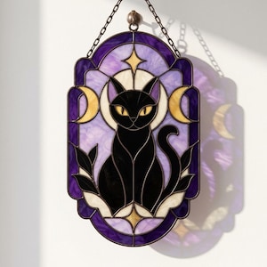 Peut inclure: Un attrape-soleil en vitrail représentant un chat noir assis au centre, entouré d'un fond marbré violet et blanc. Le motif comprend des croissants de lune jaunes et des étoiles, le tout dans un cadre sombre avec une chaîne de suspension.