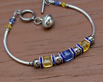 May include: A silver bracelet with a football charm and blue and yellow square beads.