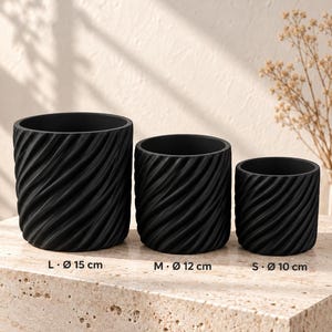 Könnte beinhalten: Drei schwarze zylindrische Pflanzgefäße mit diagonal gerippter Textur. Die Größen sind als L mit 15 cm Durchmesser, M mit 12 cm Durchmesser und S mit 10 cm Durchmesser gekennzeichnet. Jeder Topf hat ein glattes Inneres und eine matte Oberfläche.