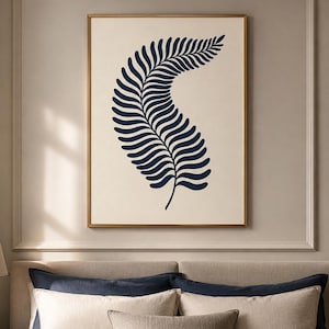 May include: A framed wall art print featuring a dark navy blue fern leaf illustration centered on a cream-colored background. The artwork is enclosed in a thin gold-toned frame, displaying a single botanical element with curved fronds.