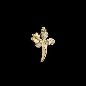 May include: A gold dagger-shaped stud earring featuring a pointed blade and a cross-guard design. The piece is embellished with four small, round, clear white stones set into the hilt and cross-guard, with a flat post backing visible.