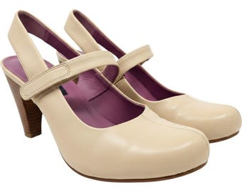 May include: A pair of cream-colored leather slingback heels featuring a rounded toe, a single adjustable strap across the instep with a hook-and-loop closure, a stacked brown wooden heel, and a contrasting deep purple interior lining.