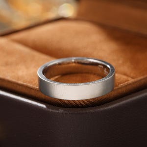 May include: A silver-toned metal ring with a flat, smooth band and a matte finish. The ring features a simple, circular design with a consistent width throughout the entire band, showcasing a clean and unadorned surface texture.