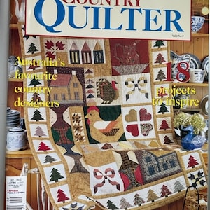 May include: A magazine cover for Country Quilter, Vol 1 No 2, featuring a patchwork quilt with a country theme. The quilt includes a rooster, houses, trees, and hearts. The text on the cover reads "Australia's favorite country designers" and "18 projects to inspire".