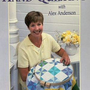 May include: A book titled "Hand Quilting with Alex Anderson" featuring a woman quilting a blue and green quilt in a hoop. The book cover also says "Six Projects for Hand Quilters".