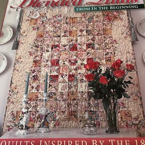 May include: A book cover titled "Blended Quilts" with floral quilt patterns. The cover features the names Marsha McCloskey and Sharon Evans Yenter. A bouquet of red roses in a glass vase and decorative candle holders are in front of the quilt.
