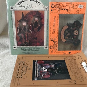 May include: Three vintage Halloween-themed cross-stitch patterns featuring witches and a jack-o'-lantern. The patterns are printed on brown paper with a white border and include instructions for stitching.
