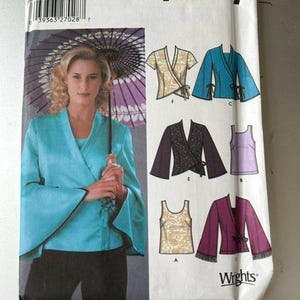 May include: A Simplicity 5347 sewing pattern envelope for a wrap-style top with flared sleeves and a sleeveless tank top. The cover features a photograph of a person wearing a turquoise wrap top and illustrations of variations in beige, blue, black, purple, and patterned fabrics.