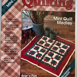 May include: A book cover for a quilting pattern titled "Mini Quilt Medley" featuring a red, white, and blue quilt with a bear paw design. The book cover also includes the text "PLAID'S Quilting" and "Bear's Paw".