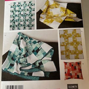 May include: Simplicity pattern 1390 OS featuring quilt designs. The designs include quilts and a pillow with patchwork patterns in shades of green, yellow, and red. The pattern is designed and printed in the USA.