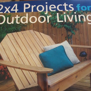 May include: The cover of a book titled "2x4 Projects for Outdoor Living" features a wooden Adirondack chair with two pillows. The chair is made of light-colored wood and has a teal and a light-colored pillow. The background shows a wooden fence.