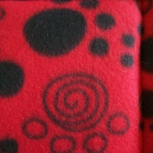 May include: Red fleece fabric with a black paw print pattern. The fabric has a soft, fuzzy texture.