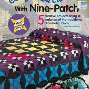 May include: A quilting pattern book titled "Going in Circles with Nine-Patch" featuring a quilt with a black, blue, white, and purple design. The book cover also includes the text "5 creative projects using a variation of the traditional Nine-Patch block." and "Designs by Lucy Fazely".