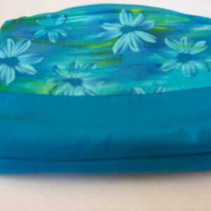 May include: A turquoise blue zippered pouch with a floral print featuring blue and green flowers on a light blue background.