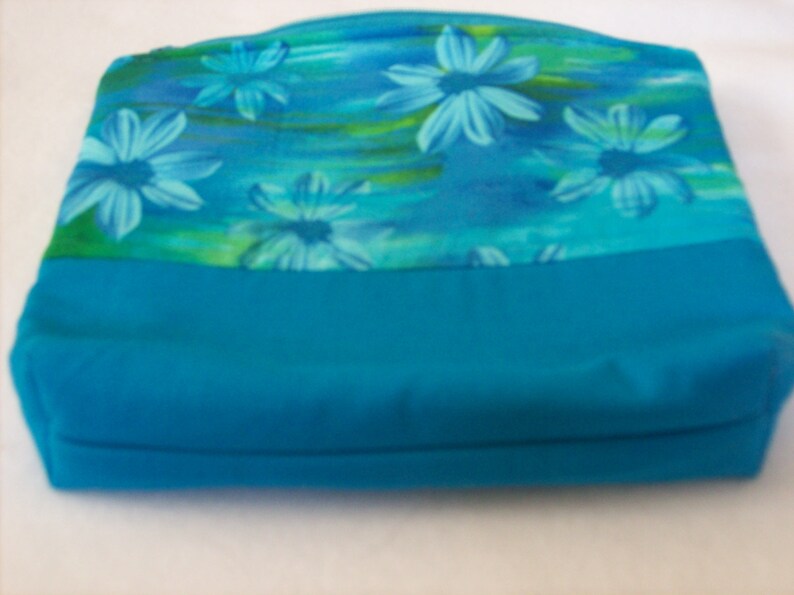 May include: A turquoise blue zippered pouch with a floral print featuring blue and green flowers on a light blue background.