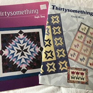May include: Two quilting pattern books with the titles "Thirtysomething" and "Thirtysomething, too!" by Gayle Bong. The first book features a quilt with a starburst design in shades of blue, pink, black, and white. The second book features a quilt with a star design in shades of yellow, blue, and white.