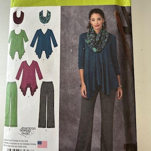 May include: Simplicity sewing pattern 1323 featuring a woman wearing a teal top and gray pants. The pattern includes designs for tops and pants. The pattern size is US 14-22.