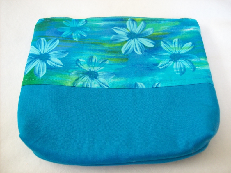May include: A turquoise zippered pouch with a blue floral print. The pouch has a solid turquoise bottom.